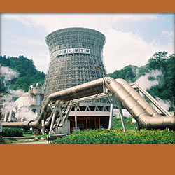 Geothermal power plant with steam rising, showcasing industrial pipes and a cooling tower surrounded by greenery.